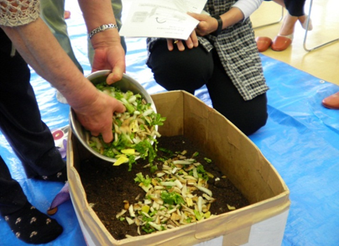ダンボールコンポストに野菜の葉っぱ部分など余った生ごみを入れている写真