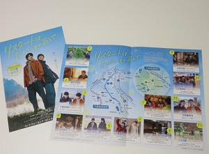 「リスタートはただいまのあとで」と書かれたパンフレットの上に、地図と多くの写真が載ったロケ地マップが開いて置かれている写真