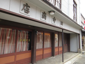 入り口の上部に田中商店と書かれ、ガラスの引き戸がある商店の外観の写真