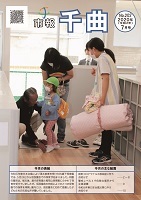 大きな荷物を持った保育士の女性が、玄関にいる児童を見守っている、2020年7月号の市報表紙