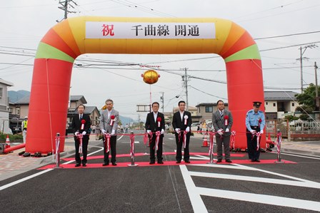 オレンジ色のアーチに「祝千曲線開通」と書かれ、テープカットが行われている写真