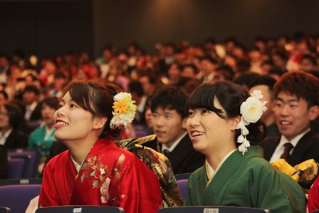 食い入るようにスクリーンの映像を見ている晴れ着の新成人女性二人の写真