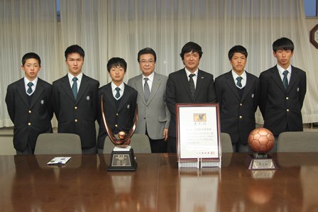 会議室の窓の前で賞状とサッカーボール型の銅のトロフィーを前に市長を真ん中に並んでいる高校生6人の写真