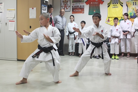 空手の型をする小学生選手と見学する選手と先生の写真
