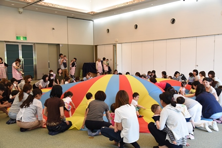 屋内に設置されたカラフルなパラバルーンの周りに集まる親子達の写真