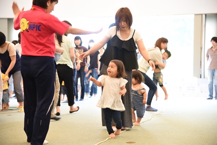 床に置いたロープの上をバランスを取りながら歩く親子達の写真