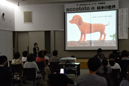 プロジェクターの前で講演をする絵本作家とそれを聞く市民の写真