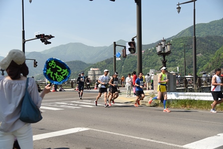 コースのコナーを曲がる選手たちと沿道でうちわをもって応援する人の写真