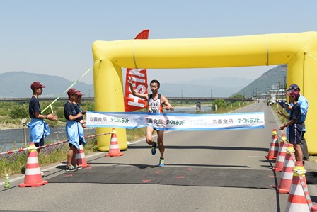 大会スタッフが持つゴールテープをきりゴールする選手一名の写真