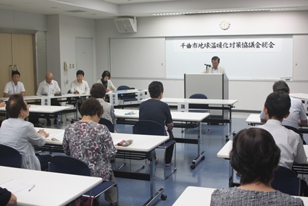 会議室で挨拶をする男性1名とそれを座って聞く大人の写真