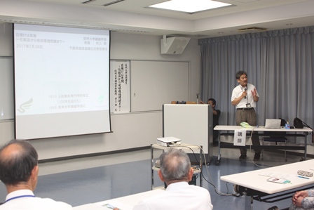 プロジェクターに資料を映しながら講演をする男性1名と講演を聞く大人達の写真