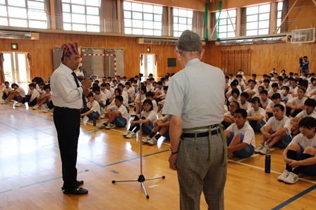 ネパール人の国連職員の男性が中学校の体育館で生徒に挨拶をしている写真