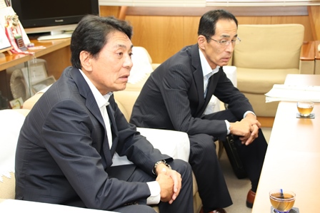 男性二人が並んで座り一人が話しかけている写真