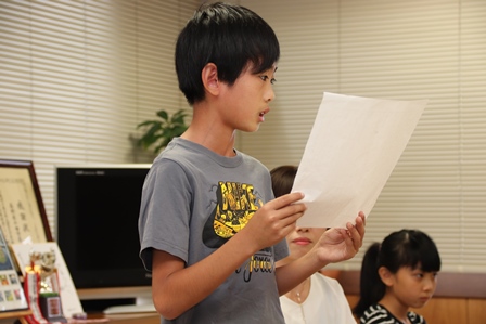 小学生の男の子が紙を持って文章を読み上げている写真