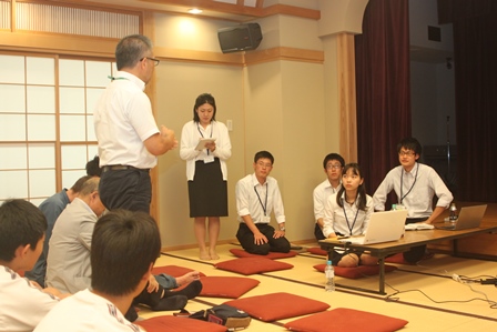 畳の部屋で大人と東京大の学生さんが向き合い一人の男性が立って学生さんに話をしている写真