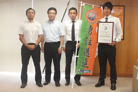 屋内でのぼり旗と一緒に移った男性四人が表彰状をもっている写真。