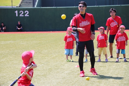 スタジアムで野球のバッティングの練習をしている男の子とボールを投げている男性の写真