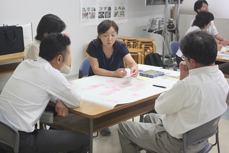 1つの机を囲み市職員4人が紙と付箋を使い話し合いをしている写真