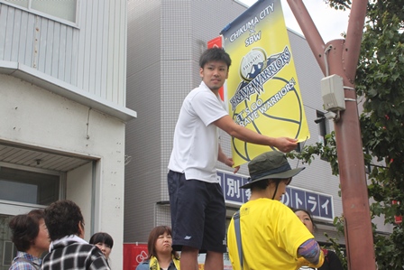 バスケットボール選手の一人が街灯に応援バナーを取り付けている写真