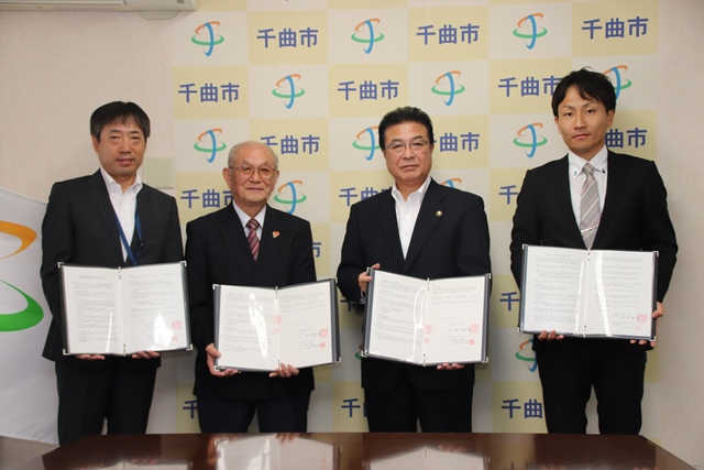 それぞれ持ったファイルを開いて見せている4人の男性の写真