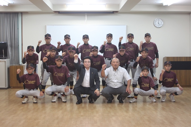 教室でこぶしを突き上げるポーズをとっている中学生硬式野球チームの集合写真