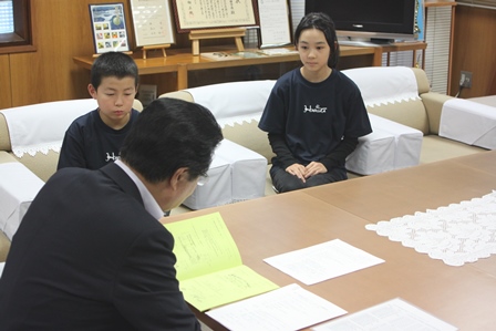 机に座って資料を見ている市長と対面して座っている男の子と女の子の写真