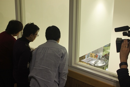 学校の給食が作られる現場を見学する大人たちの写真