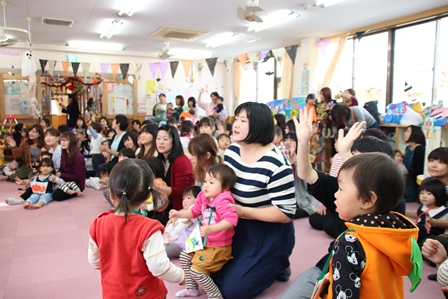 お母さんたちの膝の上んい子供が座ってみんなで催し物を見ている様子