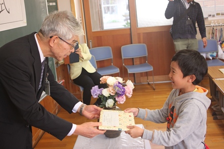 教育長から包装された本を受け取って笑顔の男の子の写真