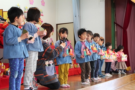 保育園のステージに並ぶ雛人形と園児たちの写真