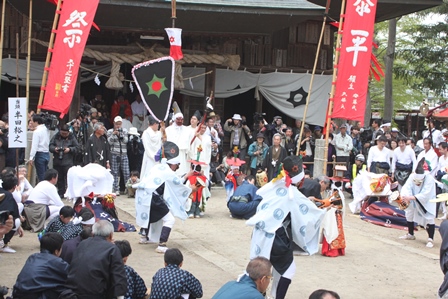 境内で御神事踊りを踊る人と見物している人々の写真