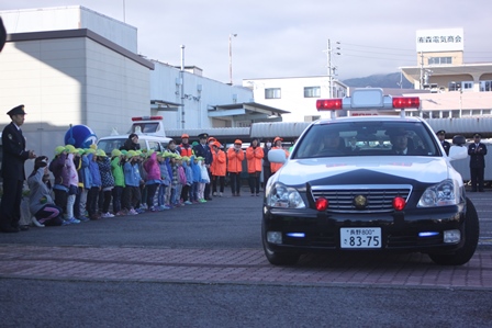 走り出すパトカーに向けて敬礼のポーズをとる園児達の写真