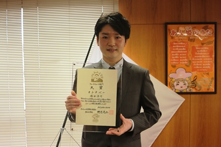 透明ケースに入った表彰状を掲げる塚田浩司さんの写真