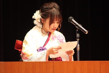 壇上のマイクに向かって原稿を読んでいる振袖姿の新成人女性の写真