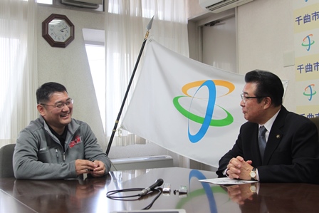 市章の旗の前でにこやかに対談する市長と中村選手の写真