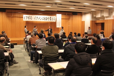 壇上の四人の話を聞いている男性たちを後ろから撮った写真