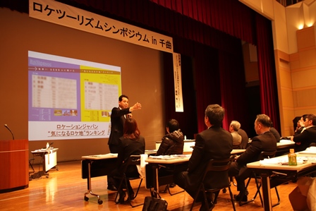 スクリーンに資料のスライドが映し出されている会場内の写真