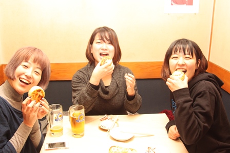 ビールとお焼きのようなものを持って笑顔の三人の女性の写真