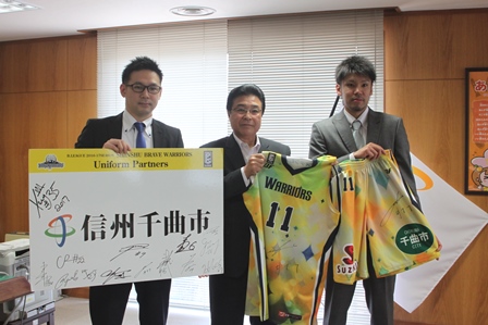 市長とヘッドコーチと選手がユニフォームをもって記念写真を取っている写真