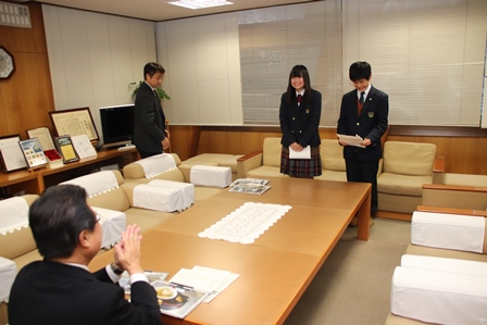 座っている市長の前でお辞儀をしている高校生二人の写真