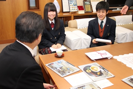 市長の前に座り作った料理のプレゼンテーションしている高校生二人の写真