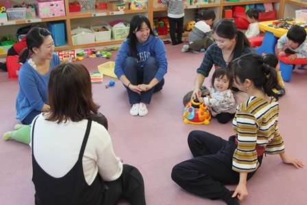 カーペットに座り円になって子どもと遊んでいる女性5人の写真