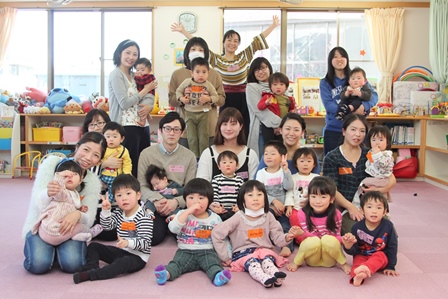 おもちゃがある室内で小さな子どもたちと保護者が集まっている写真