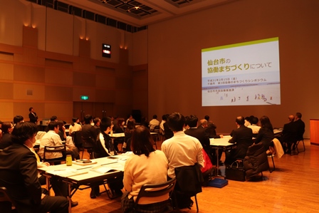 約60名の参加者がまちづくりについての発表を聞いている写真