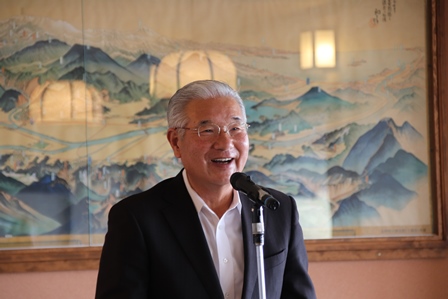 飾られている絵画の前でマイクに向かって演説をしているおじいさんの写真