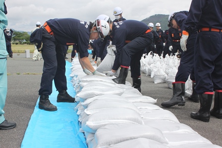 水防訓練で白い土のう袋を積み上げるヘルメットを着用した消防団員の写真
