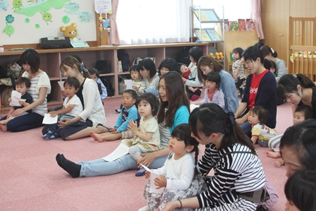 子どもを後ろから抱いて座り込む、コンサート参加者の母親達の写真