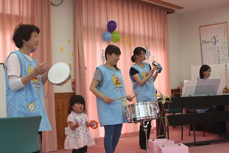 タンバリン、小太鼓、ピアノなどそれぞれの楽器で演奏している女性達と園児の写真