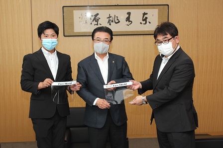 フェイスシールドの見本を手にした市長、営業部長、常務取締役が並んで立っている写真
