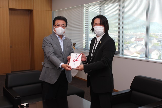 市長と理事長がカメラに向けてのし袋を見せながら記念撮影をしている写真